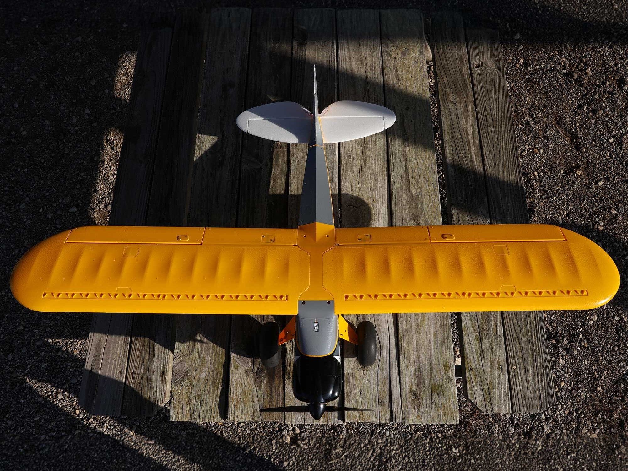 Top view of the Carbon Cub S 2 Cleetus McFarland RC airplane with a classic yellow design on a wooden surface.