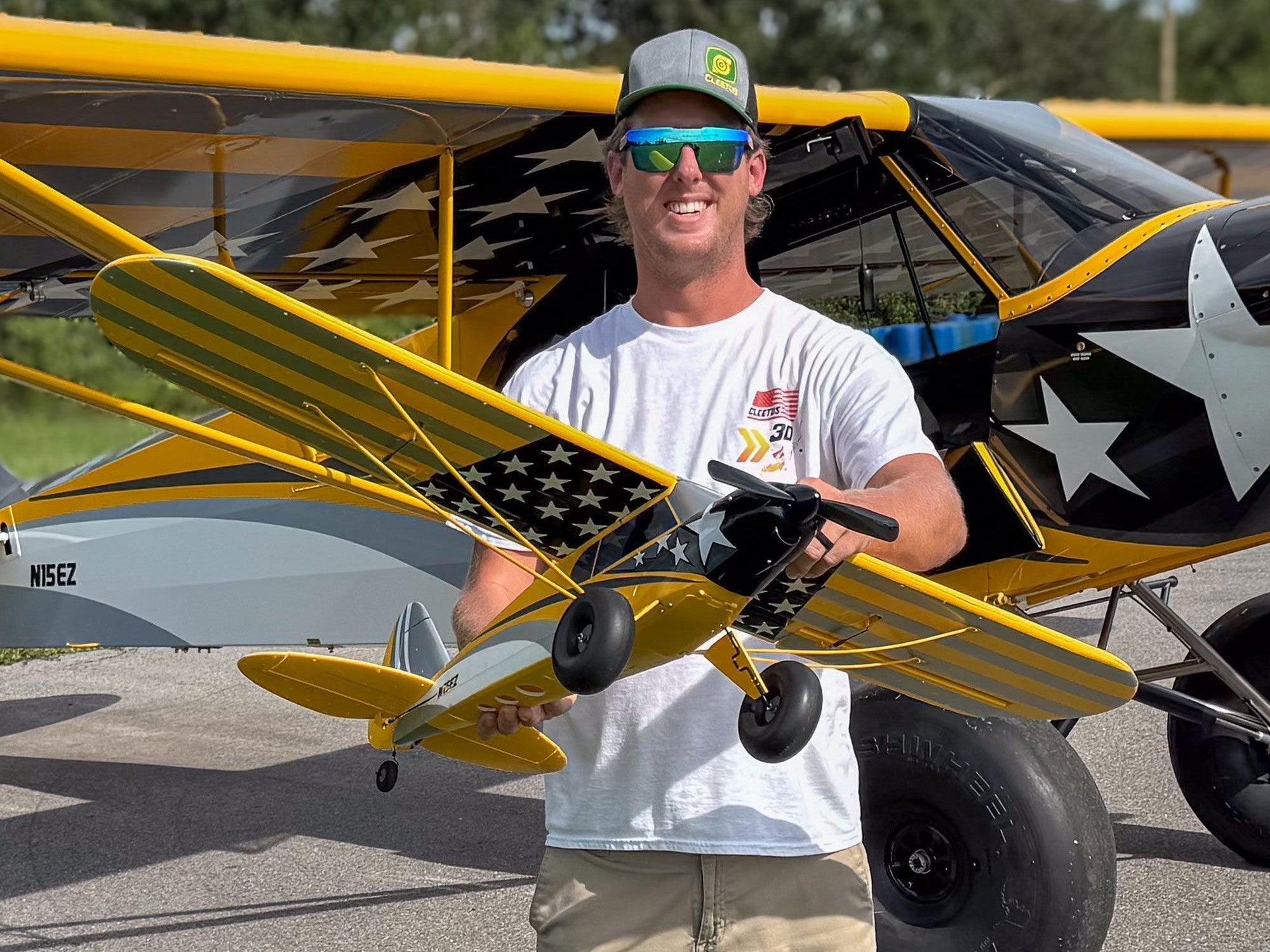 A man stands proudly holding the Carbon Cub S 2 Cleetus McFarland RC airplane next to a full-size CubCrafters aircraft.