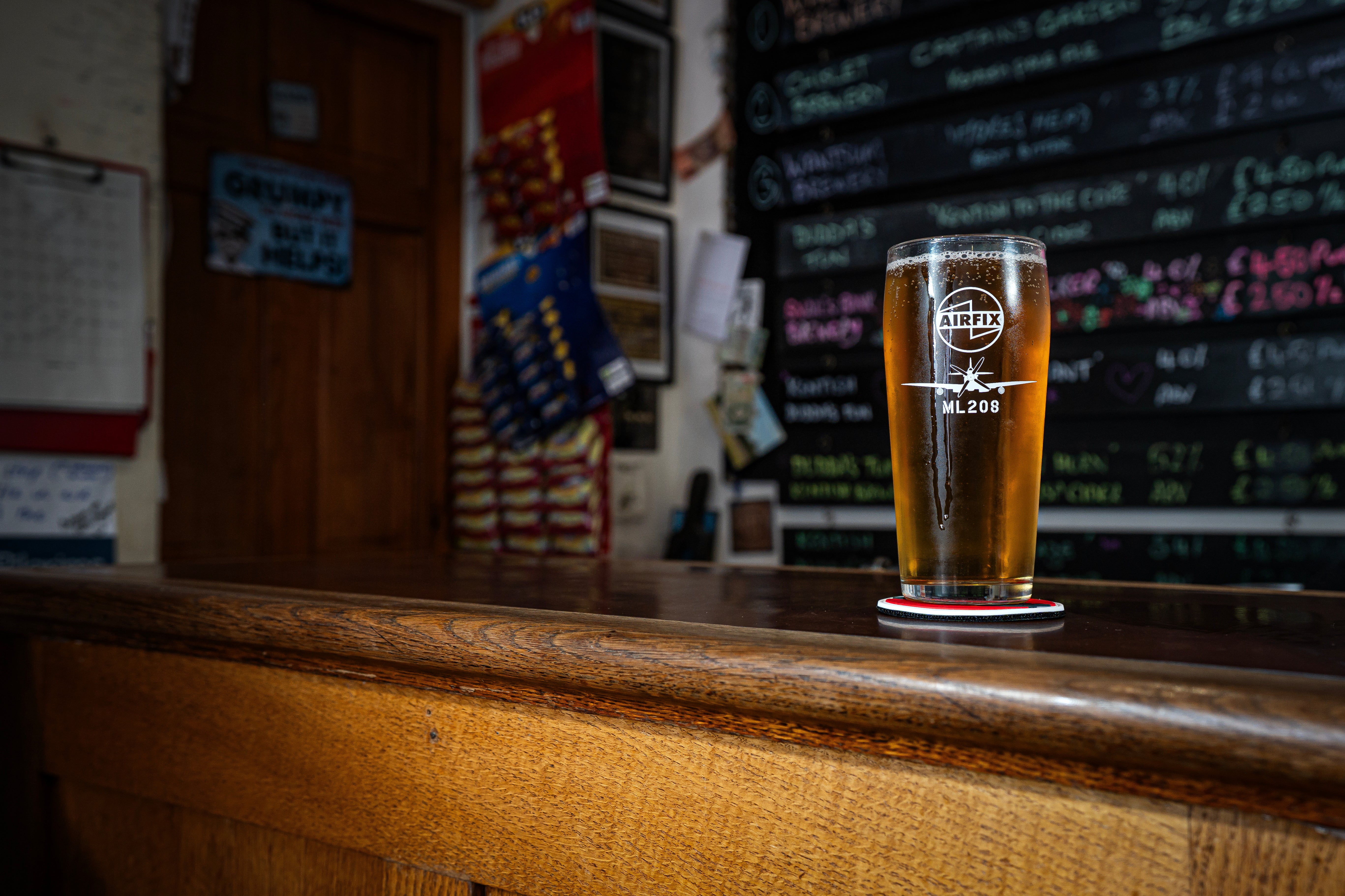 Pint glass of beer on a bar counter with a chalkboard menu in the background
