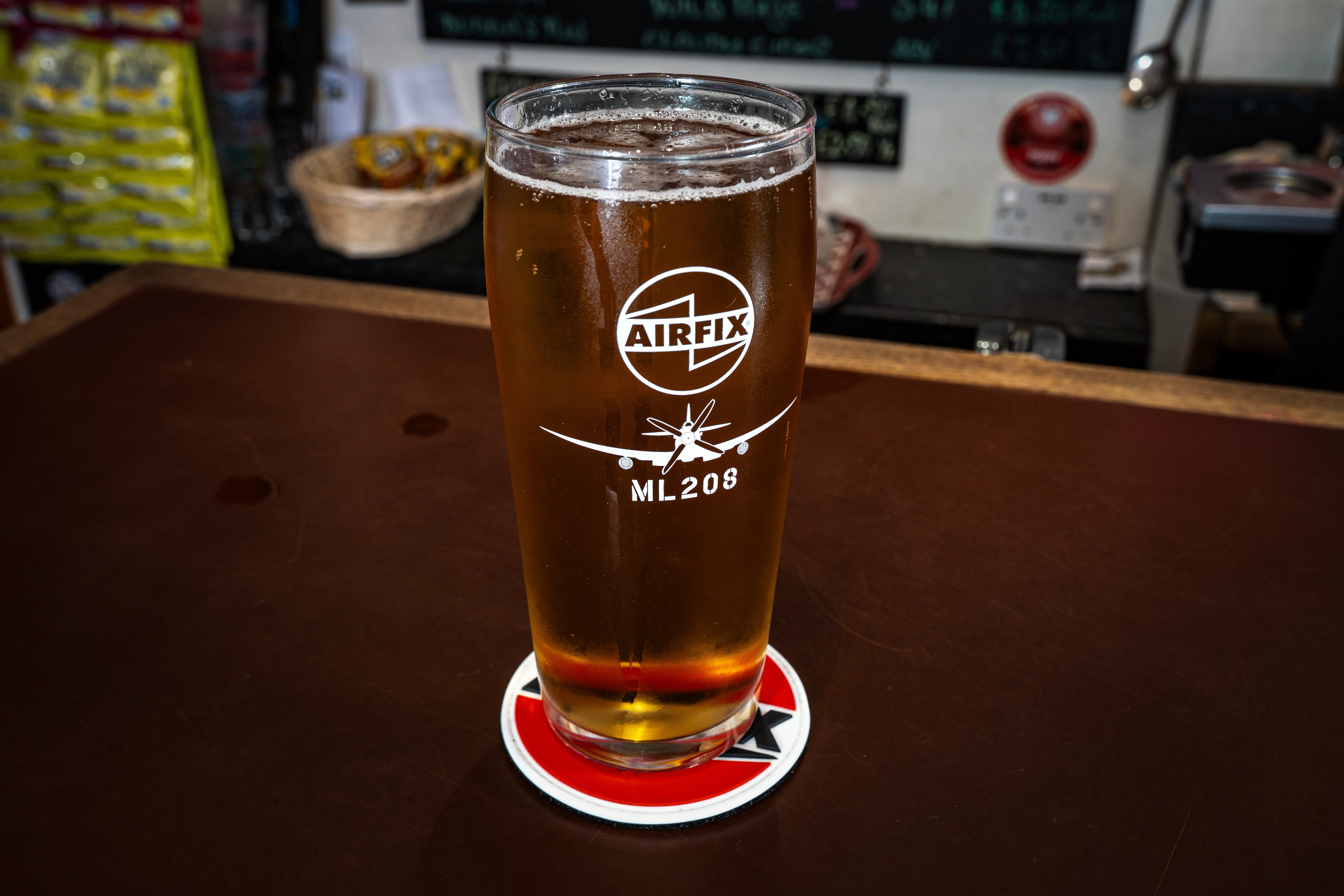 Pint glass with Airfix logo on a coaster, placed on a wooden surface.