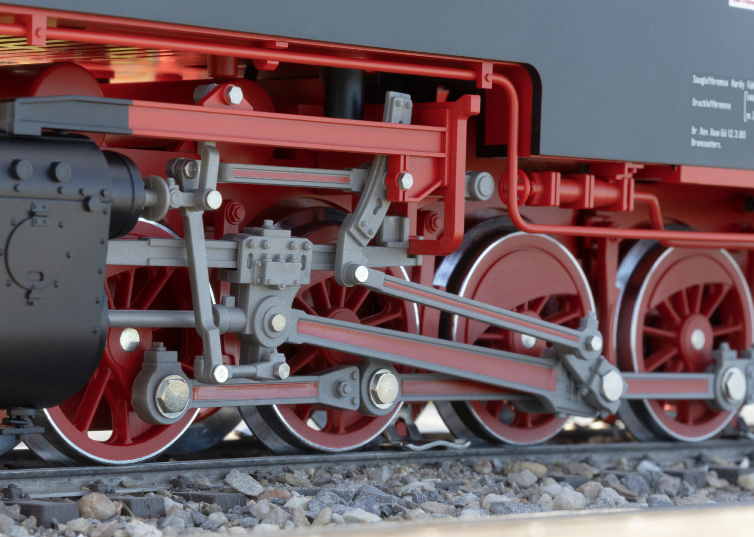 Close-up of a red steam locomotive's wheels and mechanical components on tracks.