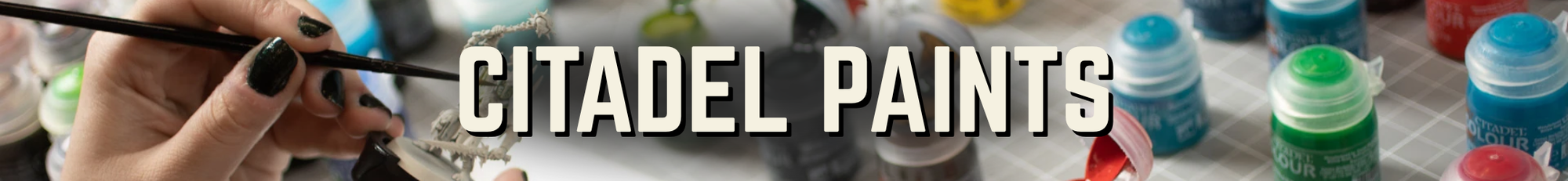 Collection of Citadel Paints with a hand holding a brush, set against a blurred background.